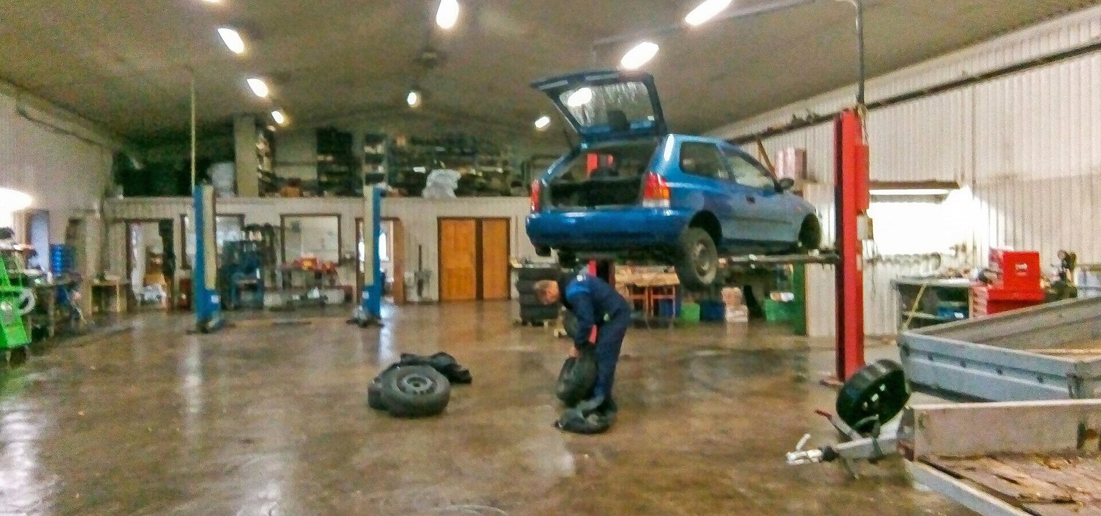 Car repair garage, Tommy & Kristers Bilverkstad, Brastad, Lysekil Municipality, Sweden. A man is changing from summer tyres to winter tyres (studded) on a blue Mazda BA 323 199